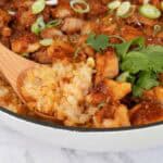 Wooden spoon scoops up a portion of cooked glutinous rice and marinated chicken from a white pan