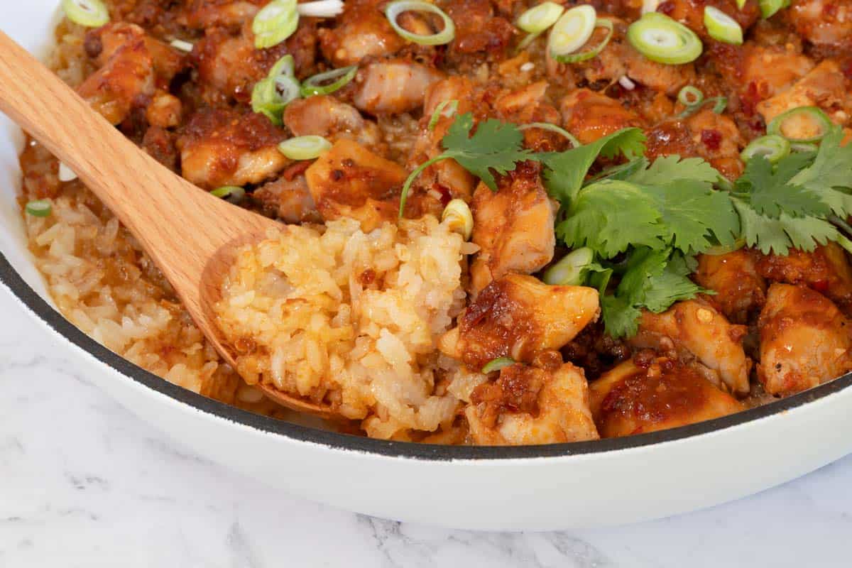 Wooden spoon scoops up a portion of cooked glutinous rice and marinated chicken from a white pan