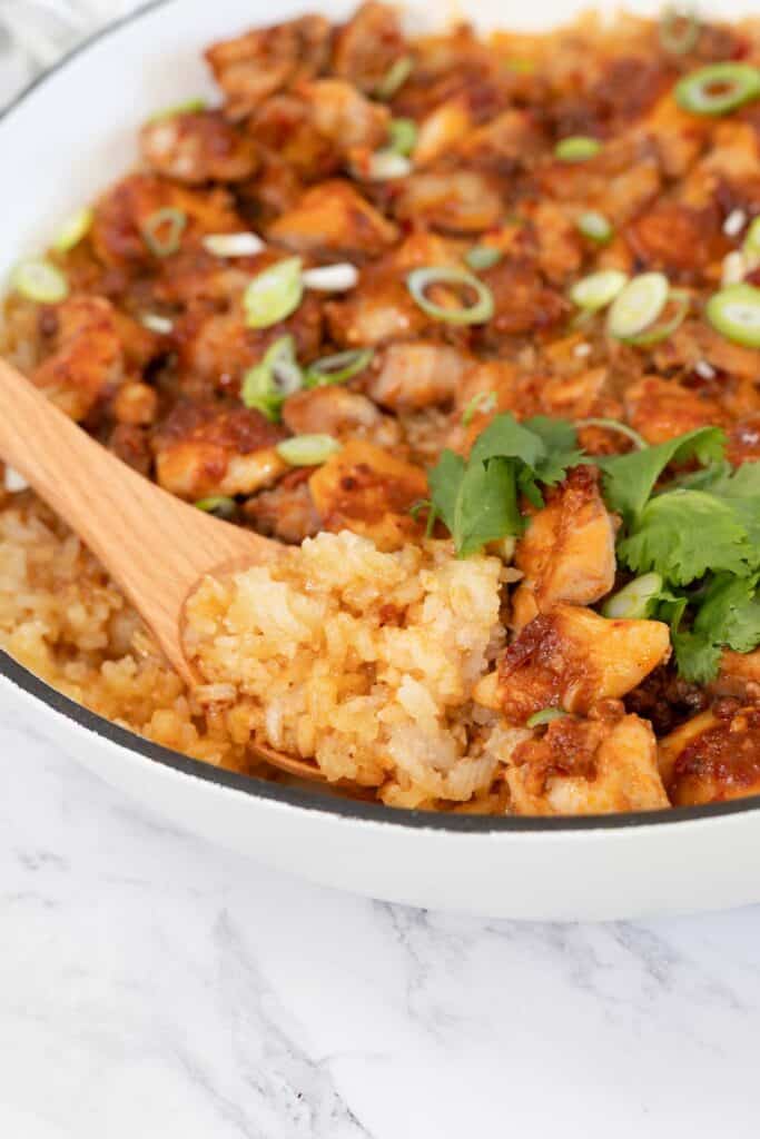 Close-up view of cooked chicken and sticky rice being served with a wooden spoon
