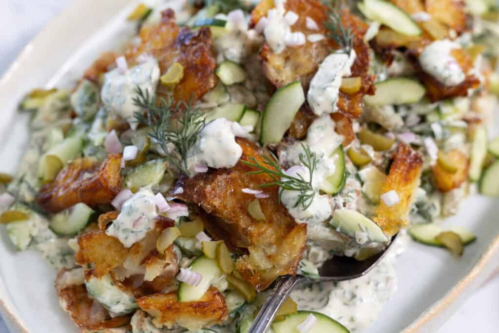 A top down view of smashed potato salad, with crispy roasted potatoes, herbs, vegetables and a creamy dressing.