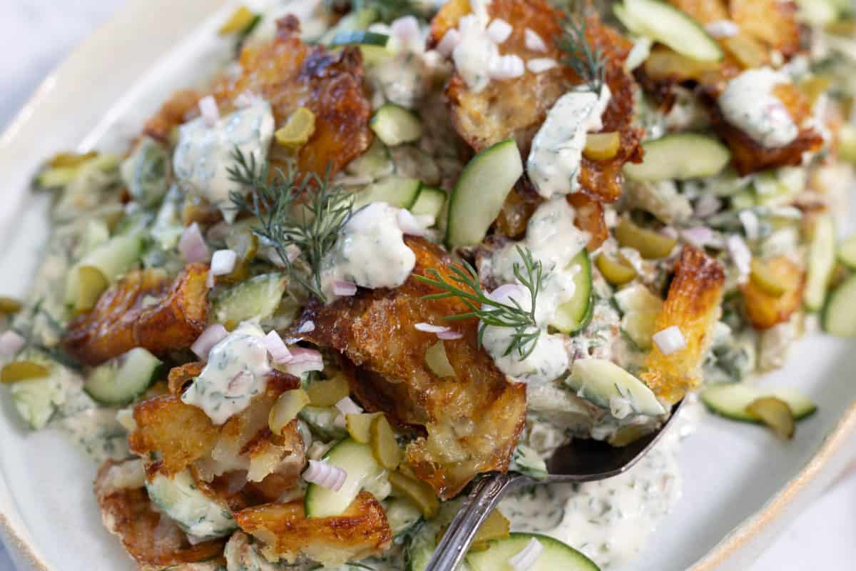 A top down view of smashed potato salad, with crispy roasted potatoes, herbs, vegetables and a creamy dressing.