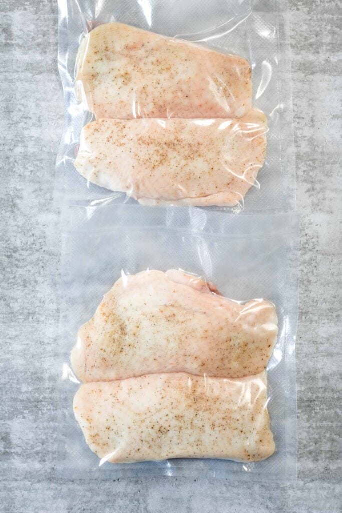 Two clear plastic bags, each containing two raw duck breasts. The duck is about to be put into a steam oven for sous vide duck breast.