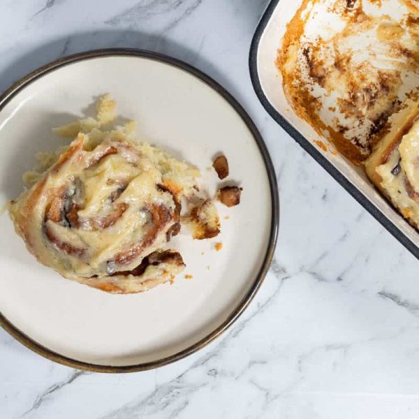 Top-down view of a soft, glazed apple cinnamon roll served on a round plate next to a baking dish filled with frosted rolls.