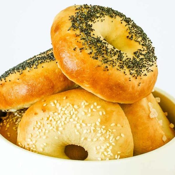 A white bowl with bagels, each topped with sesame seeds or poppy seeds or flaky salt, arranged in a pile