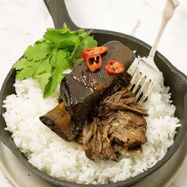 A cast iron saucepan used as a serving dish with fluffy rice and sticky Asian beef ribs