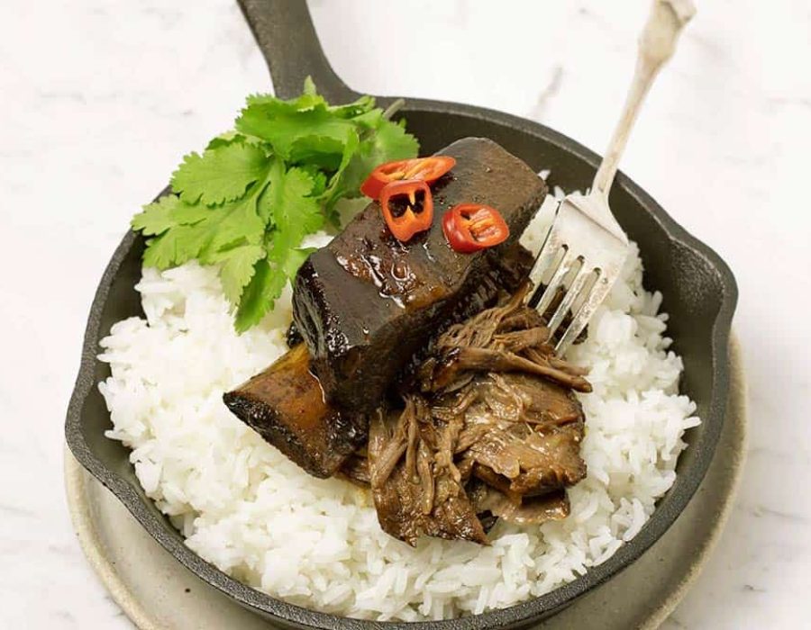 A cast iron saucepan used as a serving dish with fluffy rice and sticky Asian beef ribs