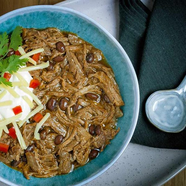a blue bowl filled with chili con carne topped with sour cream and cilantro