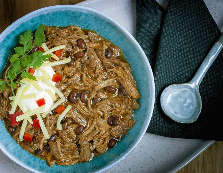 a blue bowl filled with chili con carne topped with sour cream and cilantro