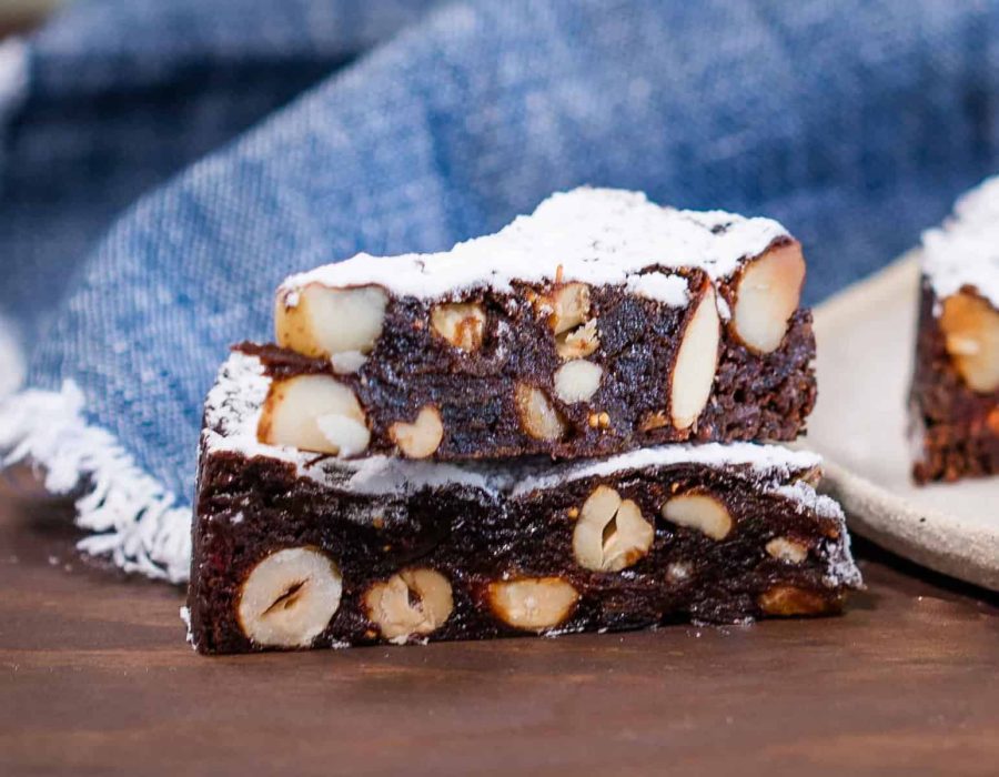 Two slices of chocolate panforte with nuts, stacked on top of each other, on a wooden surface.