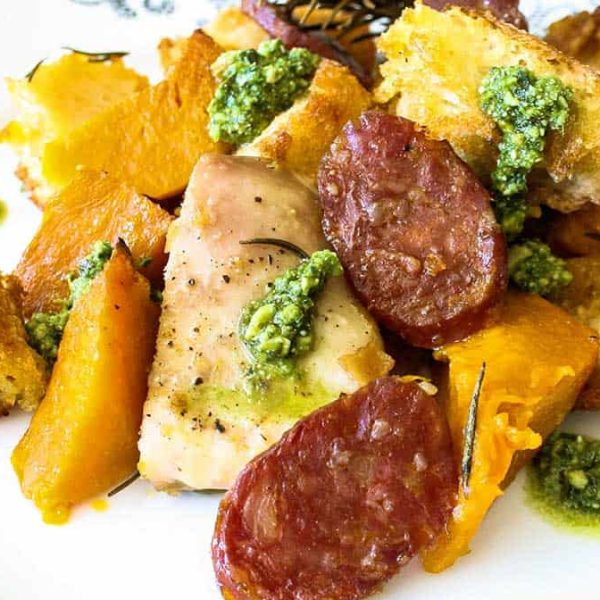 Chorizo Pumpkin Sheet Pan Dinner 1080×675 Web Chorizo Pumpkin and Chicken Tray Bake served on a patterned plate, garnished with green pesto.