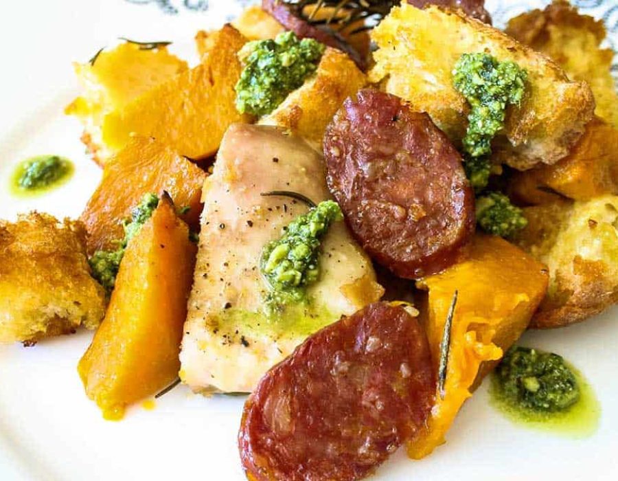 Chorizo Pumpkin and Chicken Tray Bake served on a patterned plate, garnished with green pesto.