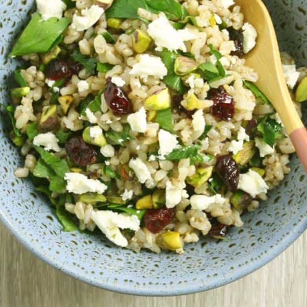 A speckled blue bowl with a rice salad with cranberries, pistachios, feta and fresh herbs and a salad server