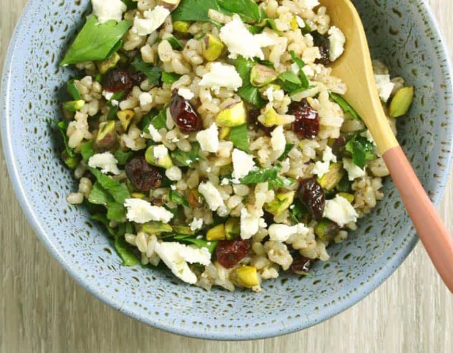 A speckled blue bowl with a rice salad with cranberries, pistachios, feta and fresh herbs and a salad server