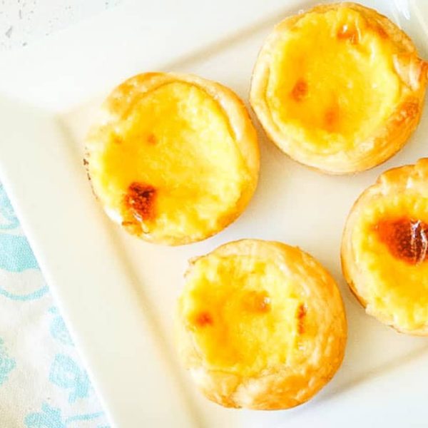 a square white plate on a patterned napkin with four Portugese Custard Tarts on it