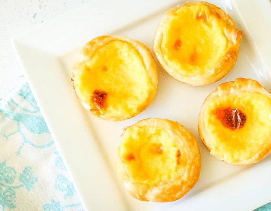 a square white plate on a patterned napkin with four Portugese Custard Tarts on it