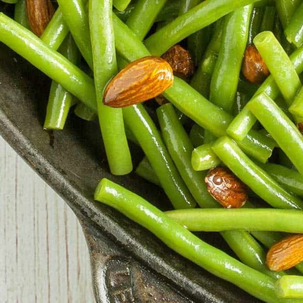 vibrant, glossy green beans and almonds in a steel baking dish