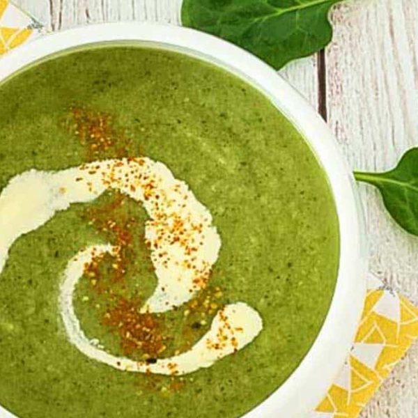 A white bowl with vibrant green soup with a swirl of cream and a sprinkle of seasoning