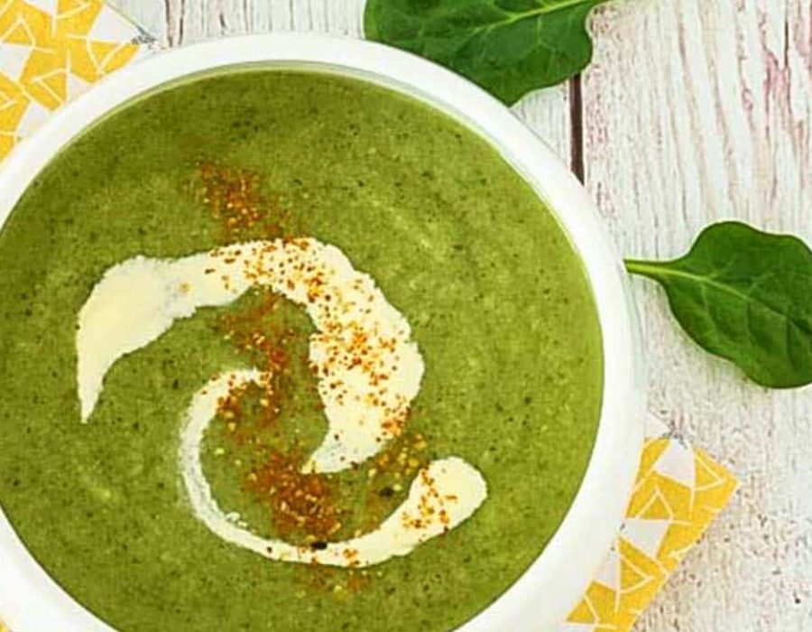 A white bowl with vibrant green soup with a swirl of cream and a sprinkle of seasoning
