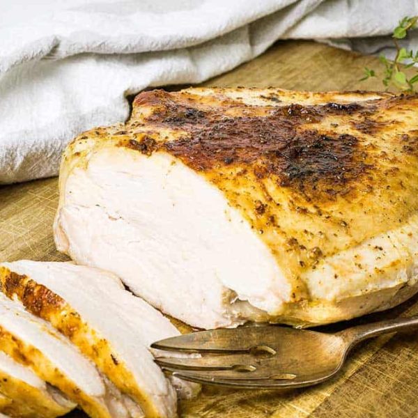 a turkey breast on a wooden chopping board with slices carved off one end and a serving fork resting beside it