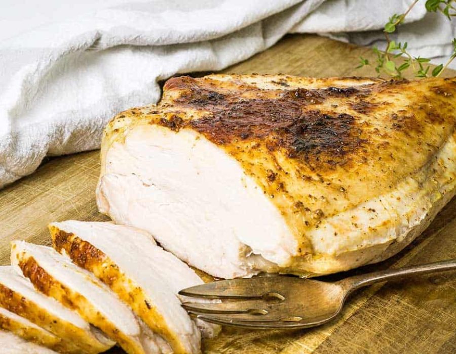 a turkey breast on a wooden chopping board with slices carved off one end and a serving fork resting beside it