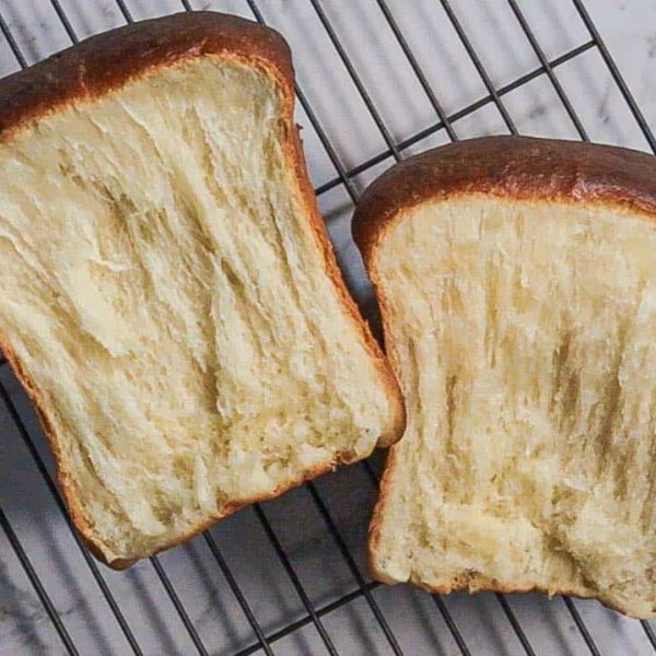 A loaf of Hokkaido milk bread, pulled apart into two pieces and resting on a metal rack.