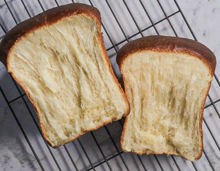 A loaf of Hokkaido milk bread, pulled apart into two pieces and resting on a metal rack.