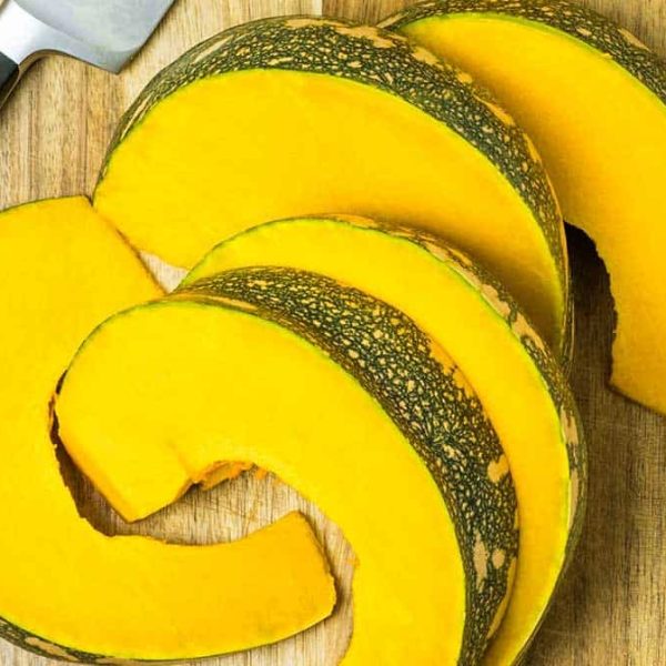 pumpkin cut into wedges, on a wooden board with a knife next to it