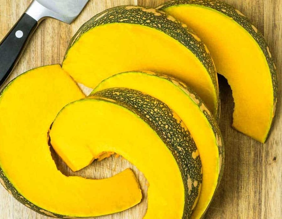 pumpkin cut into wedges, on a wooden board with a knife next to it