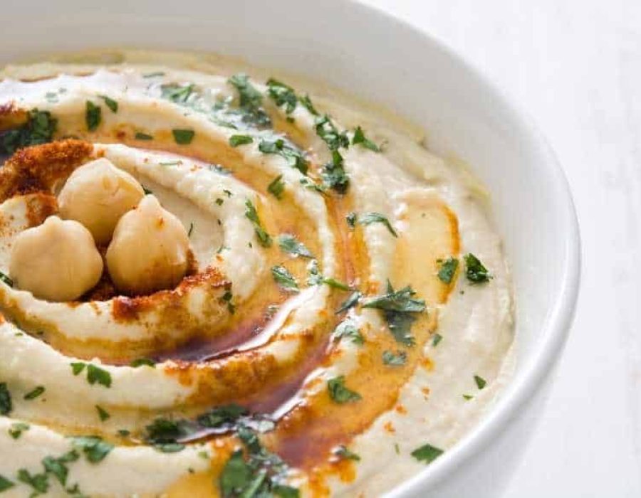 a white bowl with swirled hummus, parsley and paprika on top