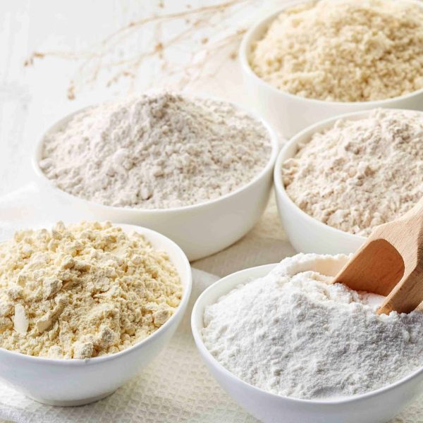 Bowls of various gluten free flour (chick peas, rice, buckwheat, amaranth seeds, almond) on white wooden background