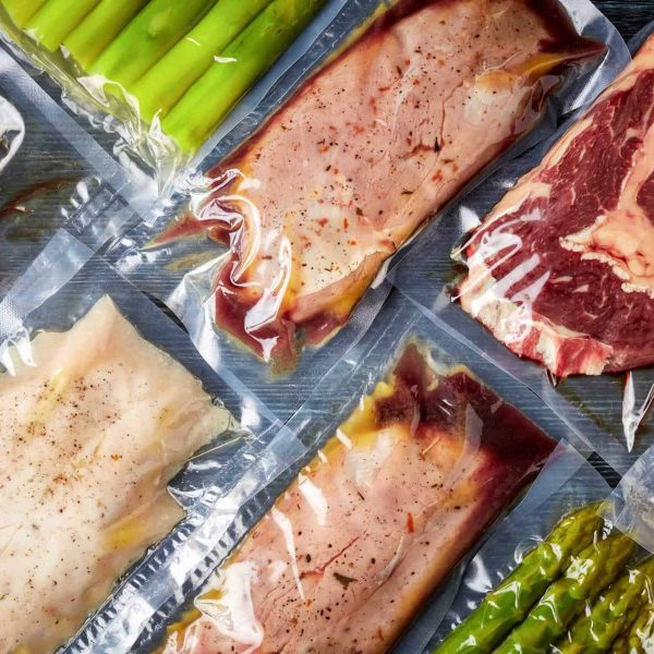 Duck breast, chicken breast, beef steak and asparagus vacuum sealed ready for sous vide cooking, on black background, top view