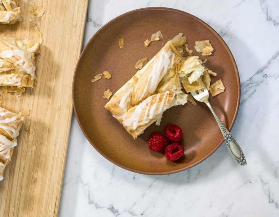 A slice of lemon cheesecake Danish on a plate with fresh raspberries.