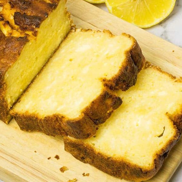 lemon ricotta steam oven cake, resting on a wooden board with two slices cut from the end of the loaf