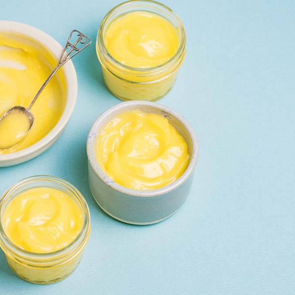 jars and dishes with lemon curd and a decorative spoon on a blue board with a halved lemon