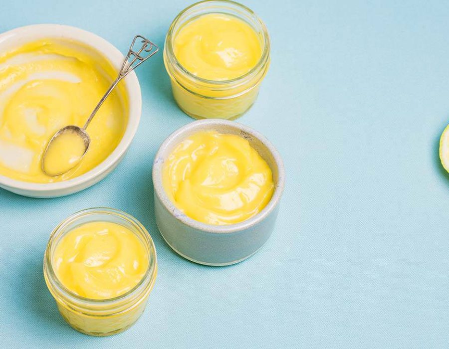jars and dishes with lemon curd and a decorative spoon on a blue board with a halved lemon