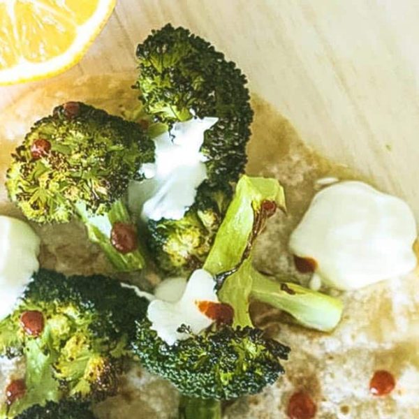 Steam oven lemon roasted broccoli florets on a pita bread with a halved lemon, white dressing and drops of chilli sauce