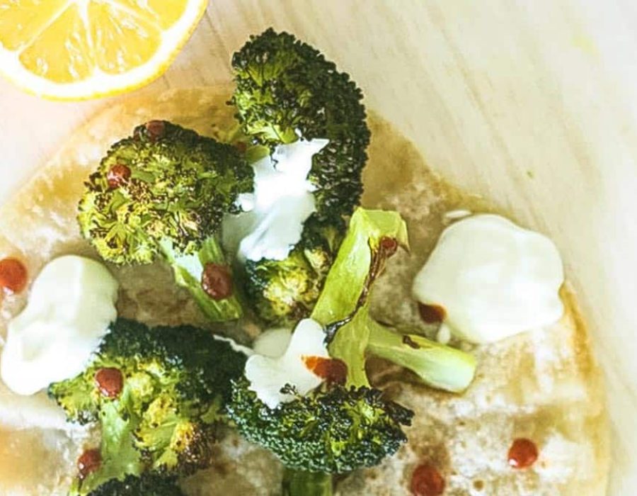 Steam oven lemon roasted broccoli florets on a pita bread with a halved lemon, white dressing and drops of chilli sauce