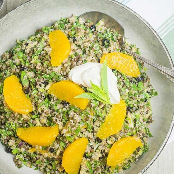 An ornate handled spoon in a bowl with a lentil herb and grain salad, on a folded green and white striped towel with a ramekin partially visible.