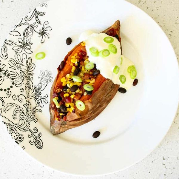 A loaded sweet potato stuffed with beans and corn, topped with sour cream garnished with sliced green onions on a patterned plate.