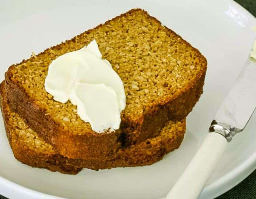 zoomed in image of two thick slices of pumpkin bread with a blob of cream cheese on top and a knife beside them on a white plate