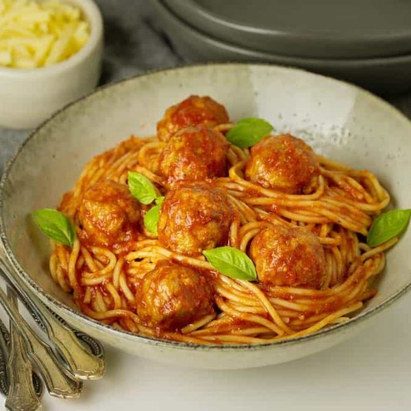 A serving bowl with saucy spaghetti and meatballs garnished with herbs