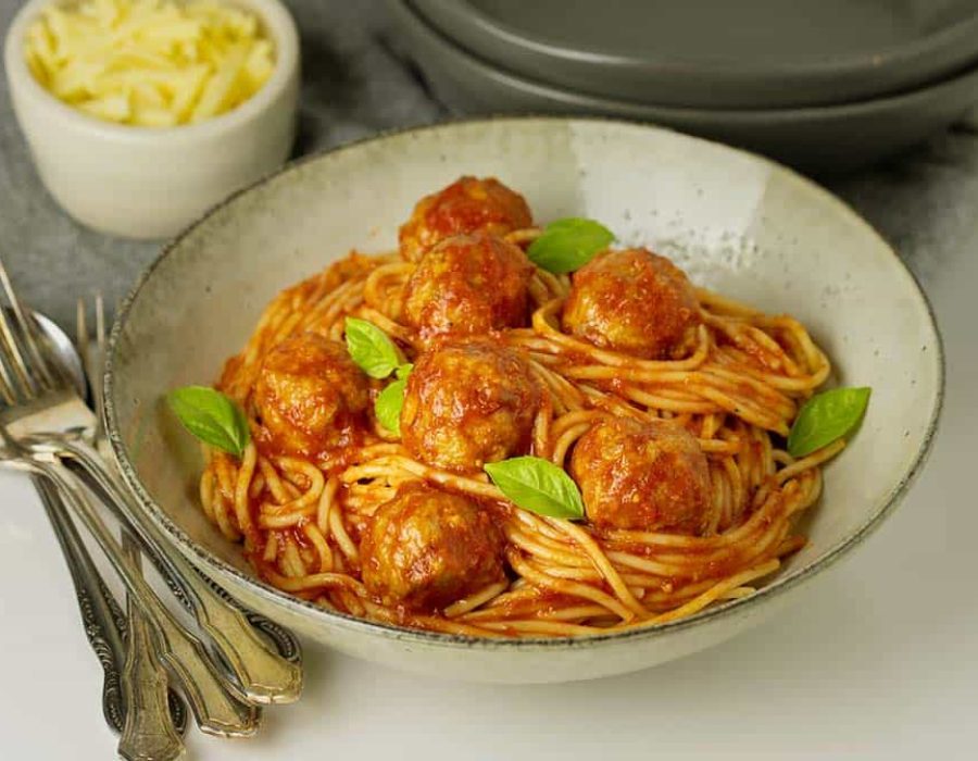 A serving bowl with saucy spaghetti and meatballs garnished with herbs