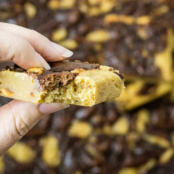 a close up image of a Nutella blondie being held between a person's fingers; a bit has been taken from the blondie