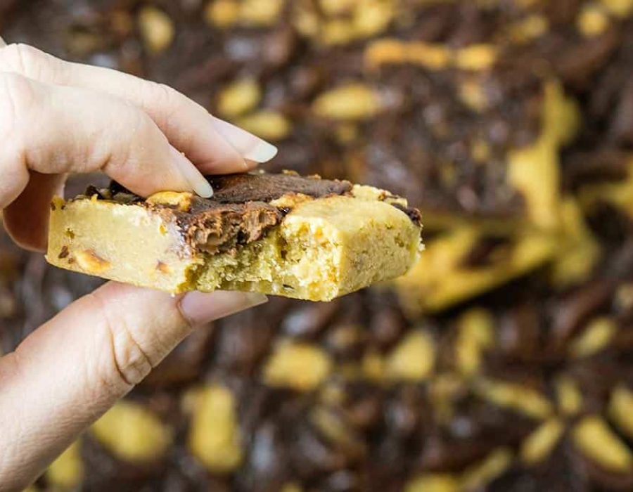 a close up image of a Nutella blondie being held between a person's fingers; a bit has been taken from the blondie