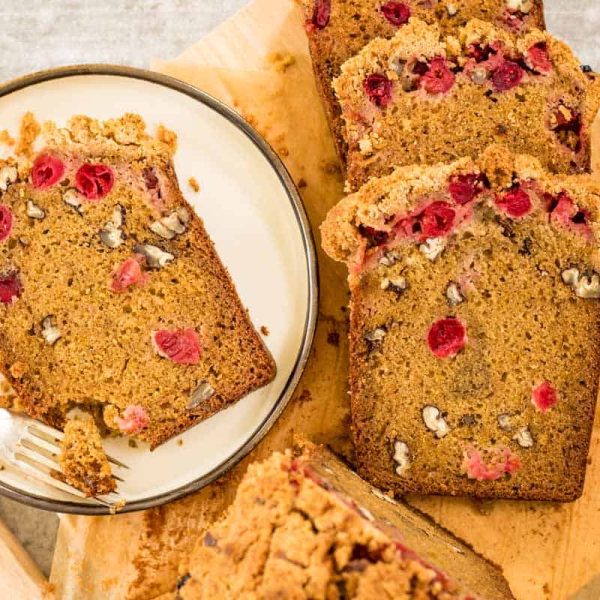 Orange Cranberry Cake Hero 2 A cream colored plate with a slice of orange cranberry cake and a silver fork. There are slices of the same cake alongside the plate on a wooden board.