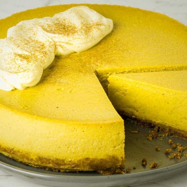 a pumpkin cheesecake with a piece removed and another piece cut on the plate to show the inside