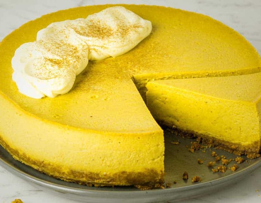 a pumpkin cheesecake with a piece removed and another piece cut on the plate to show the inside