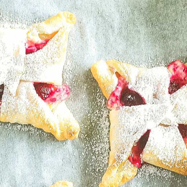 a close up image of two pastries with a raspberry cheesecake filling dusted with icing sugar
