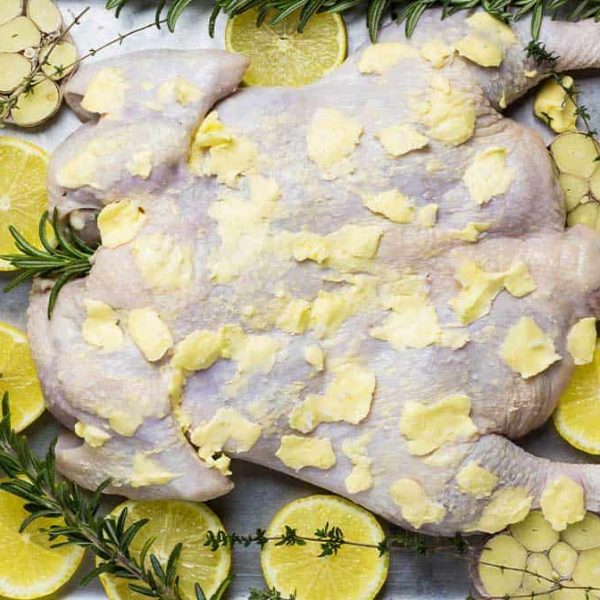 A raw, whole, butterflied chicken ready to bake in a steel dish with lemon, garlic, herbs and butter