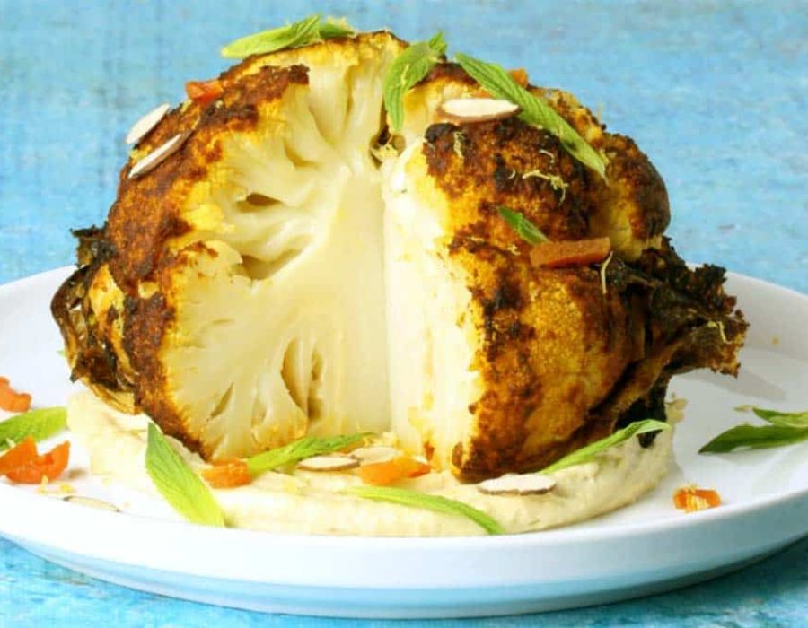 a roasted cauliflower, with a wedge cut out of it, on a white plate